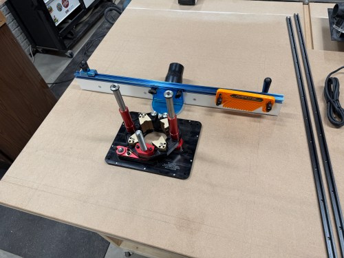 Router station setup with a lift and fence on a work table, showing precision tools and measuring instruments.