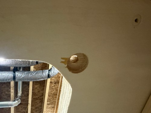 Close-up of a circular hole cut into a wooden surface, showing wood fibers and some markings around the edge.