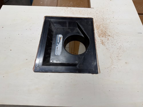 A close-up view of a dust collection port mounted on a wooden table surface, surrounded by wood shavings.