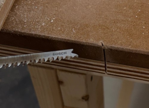Close-up of a saw cutting through a wooden surface, showing fine wood shavings and a Bosch blade.